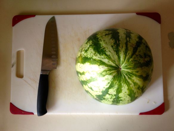 Half of a watermelon on a cutting board with a santoku knife