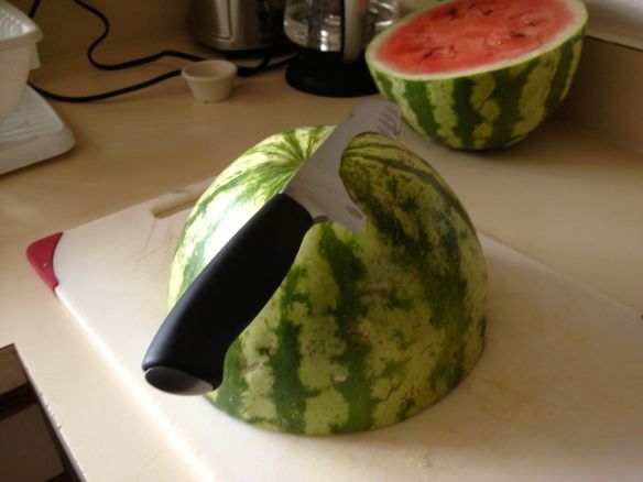 Watermelon half being shaved with a santoku kinfe