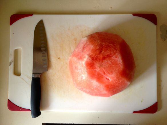 Watermelon without it's rind on a cutting board with santoku knife